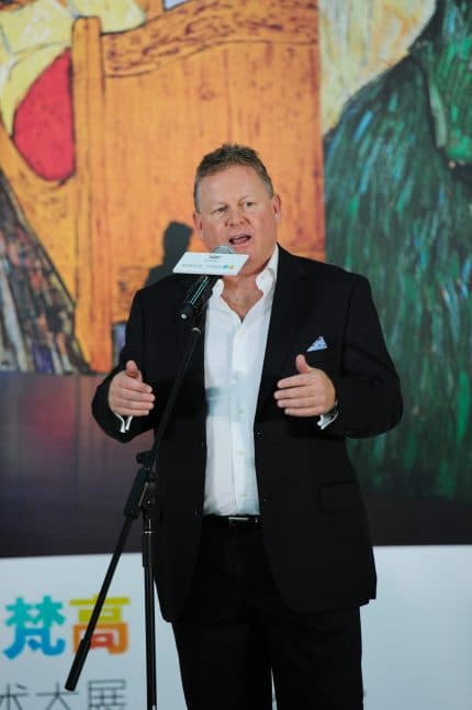 Bruce Peterson speaking into microphone in front of projected images of Van Gogh's artwork